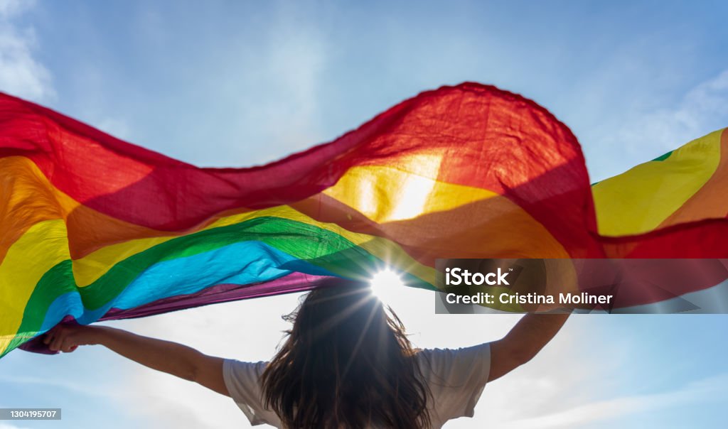 Young woman waving lgbti flag Picture of a young woman waving lgbti flag under the sky LGBTQIA Rights Stock Photo