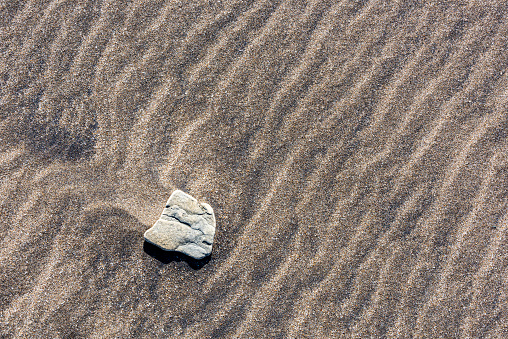 Single small white stone on brown sand on the seashore in Turkey.