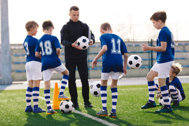 istock Young coach teaching kids on football field. Trainer explains to schoolboys training rules. Football coach coaching children. Soccer football training session for children. Football tactic education. 1304199025