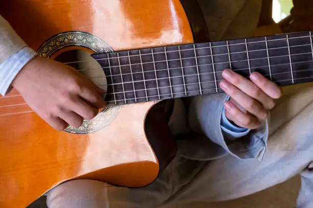detail of the hands of a white boy playing the Spanish guitar.