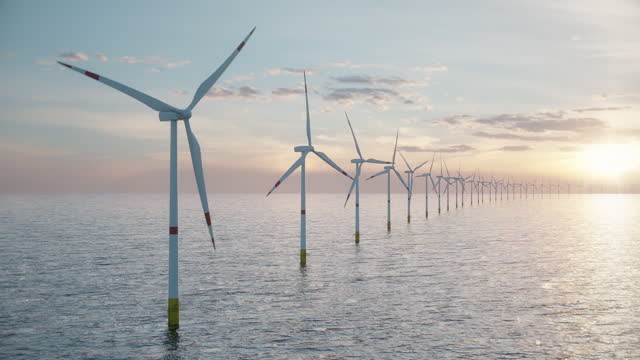 long row of offshore wind turbines in the sea against low sun