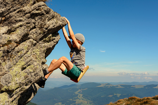 The boy is engaged in mountaineering, a child climbing a rocky mountain, a brave boy.2020