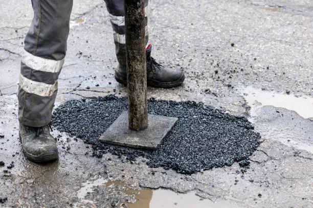 Photo of worker pushing bitumen asphalt in the hole. road repair and maintenance