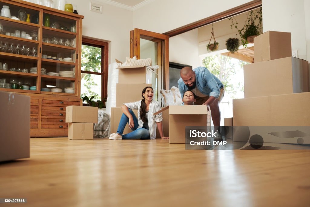 A journey well shared it a journey well enjoyed Shot of a husband pushing his toddler in a moving box while the wife relaxes in the background in their new home Mortgage Loan Stock Photo