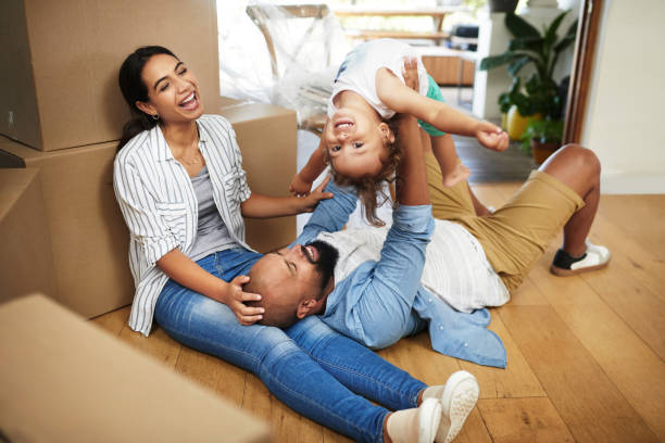 Rise by lifting others Shot of a young family of three relaxing on the floor of their new home beside moving boxes while the father lifts his toddler up in the air unpacking stock pictures, royalty-free photos & images