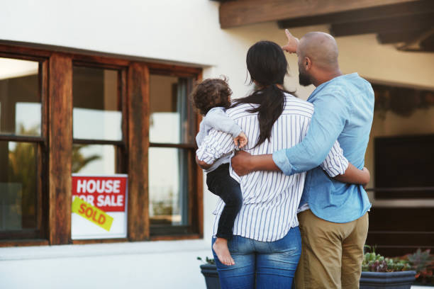 A family doesn't need to be perfect, it just needs to be united Shot of a young family of three facing their new home outside with a sold sign in the window file the father points towards the home for sale sign photos stock pictures, royalty-free photos & images