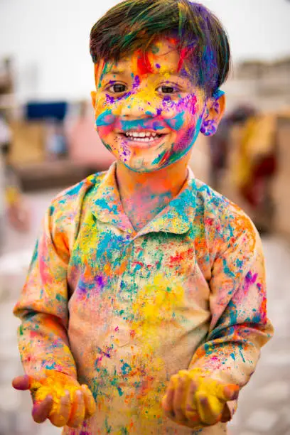 Photo of Indian little boy covered with colorful powders at Holi festival.