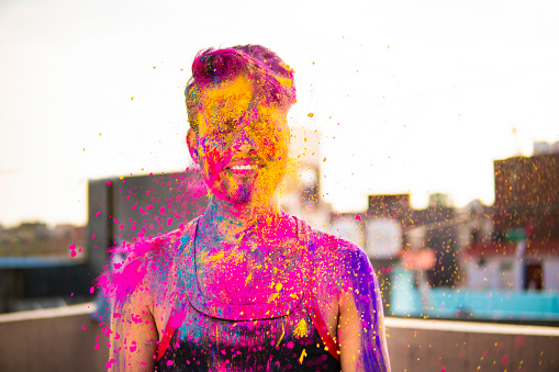 Outdoors image of an Asian/ Indian happy young man celebrating Holi festival with color powder.