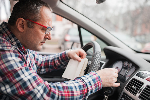 Hombre con anteojos revisando su coche y escribiendo cosas al sentarse en el asiento del conductor photo