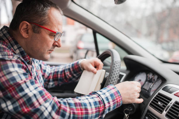hombre con anteojos revisando su coche y escribiendo cosas al sentarse en el asiento del conductor - kilómetro fotografías e imágenes de stock