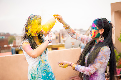 Outdoor image of Asian / Indian happy, beautiful sister in Indian dress celebrating the Holi festival together with color powder.
