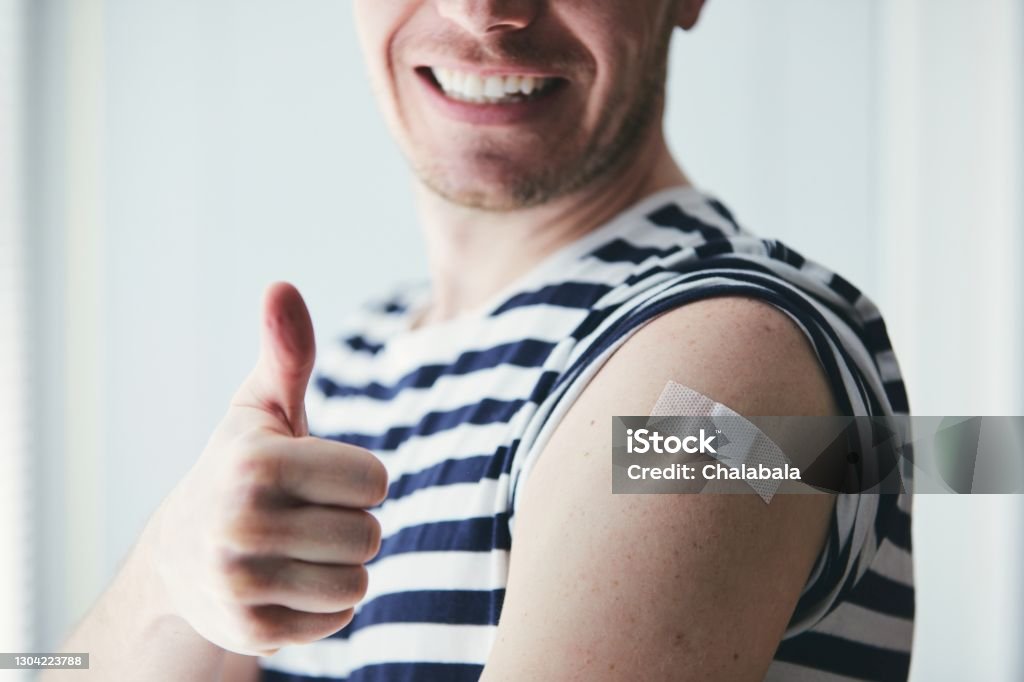 Happy man after vaccination Happy young man showing thumb up and his arm after vaccination. Themes prevention, vaccine and health care during pandemic covid-19. Vaccination Stock Photo