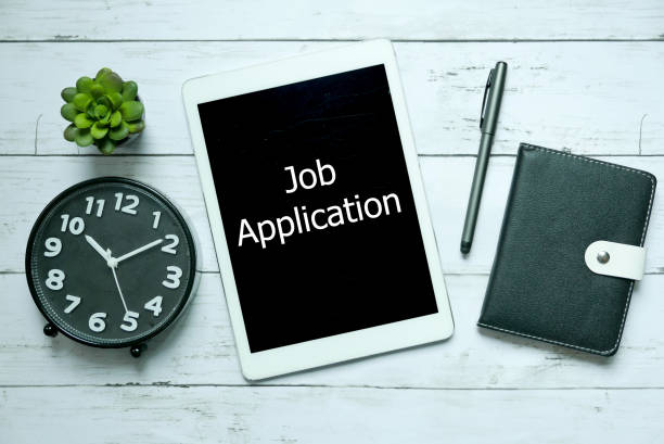istock Online digital technology job application concept.Top view of clock,plant,notebook,pen and tablet written with Job Application on white wooden background. 1304225131