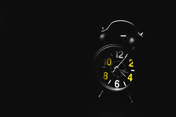 Photo of Black round modern alarm clock on black background with copy space. The concept of insomnia and night anxiety