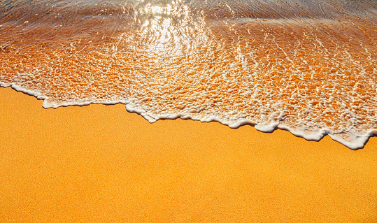 Photo of gentle ocean waves washing over the golden sand of a tropical beach