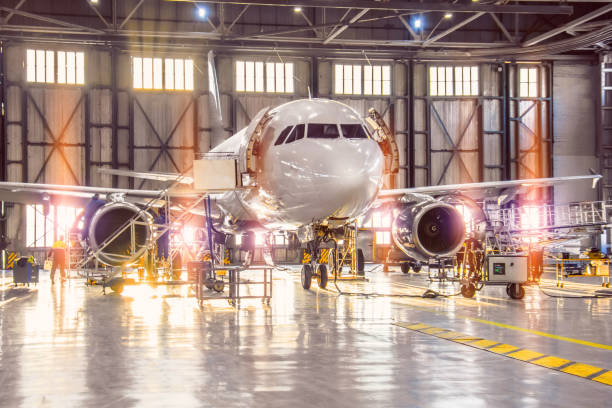 inspection à grande échelle de tous les systèmes d’aéronefs dans le hangar de l’aéronef par des mécaniciens travailleurs et d’autres spécialistes. lumière vive à l’extérieur de la porte de garage. - transport aérien photos et images de collection