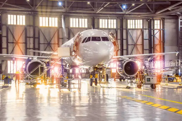 Photo of Large-scale inspection of all aircraft systems in the aircraft hangar by worker mechanics and other specialists. Bright light outside the garage door.