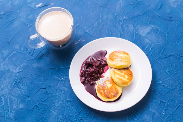 frühstück und leckeres konzept - pfannkuchen aus hüttenkäse mit marmelade, blauem hintergrund. - cheesecake syrup cottage cheese cream stock-fotos und bilder