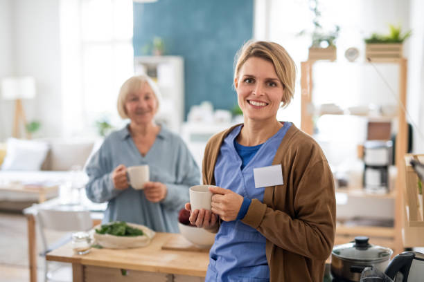 Senior woman with caregiver or healthcare worker indoors, drinking tea in kitchen. Portrait of senior woman with caregiver or healthcare worker indoors, drinking tea in kitchen. home caregiver stock pictures, royalty-free photos & images