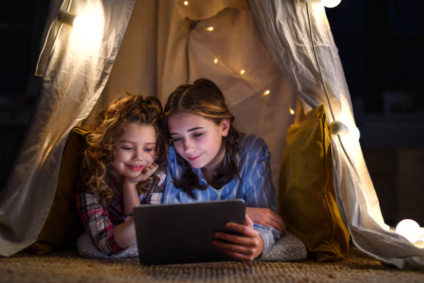 istock Sisters indoors at home, using tablet in pajamas. Lockdown concept. 1304232914