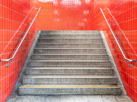 A personal perspective of an empty, concrete staircase, surrounded by old-fashioned bright red tiles.