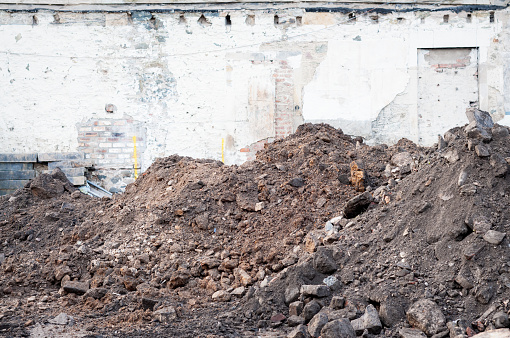 Dirt, dust, bricks and stone among piles of rubble outside a building during demolition.