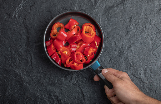 Male hand holding pan of sliced red bell peppers on black background. High quality photo