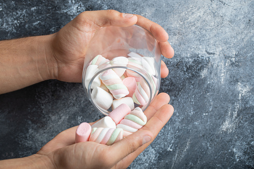 Female hands holding glass jar of marshmallows on marble background. High quality photo