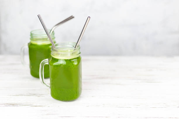 zwei gläser gefüllt mit krautgrünem detox-smoothie mit strohhalmen - chlorophyll green smoothie smoothie vegetable stock-fotos und bilder