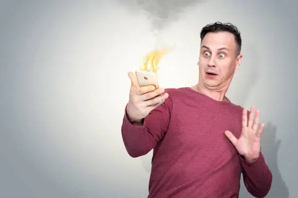 Photo of Frightened and surprised man with smartphone on fire in his hand. The situation with fire phone batteries.
