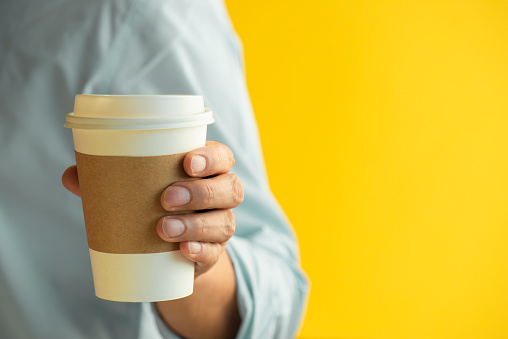 Man holding disposable coffee cup, orange background.