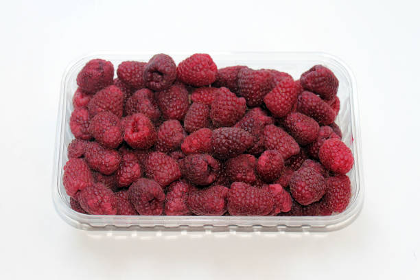 Fresh organic raw raspberries fruit pile in plastic container isolated on white background