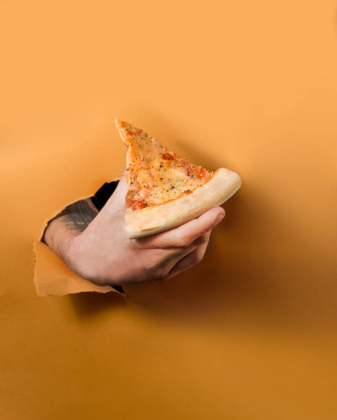 istock Hand from the background holds a slice of pizza. Torn background concept 1304258047