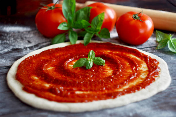 istock Raw pizza dough with tomato sauce and basil leaves. Selective focus 1304258109