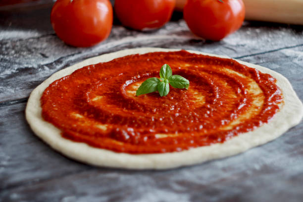 istock Raw pizza dough with tomato sauce and basil leaves. Selective focus 1304258114