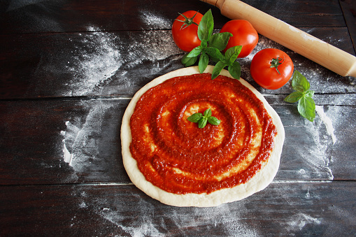 Raw pizza dough with tomato sauce and basil leaves. Top view