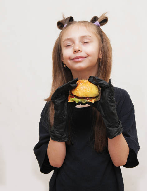 Cute little girl with black gloves eats hamburger.