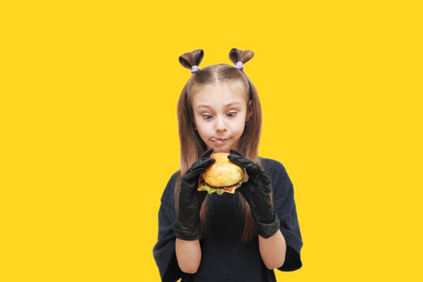 Cute little girl with black gloves eats hamburger.