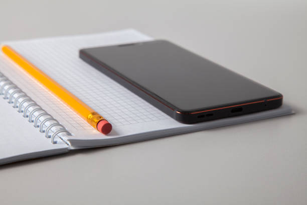 istock Open notebook, pencil and mobile phone laid out on white isolated background 1304263793