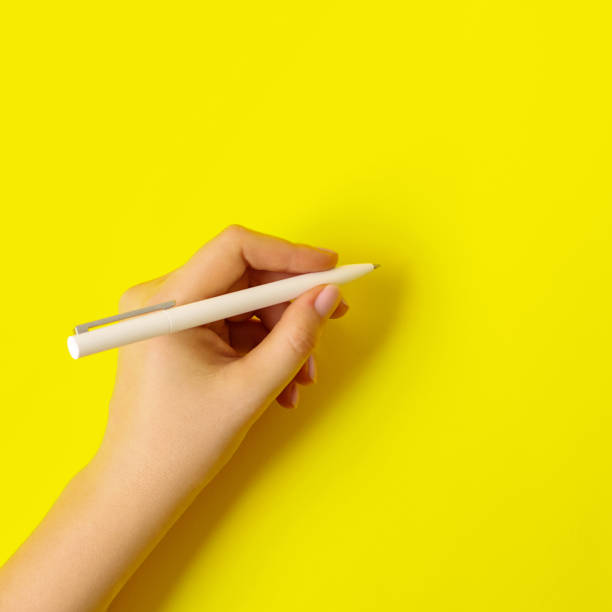 istock Female hand with a white pen on a yellow background. 1304264037