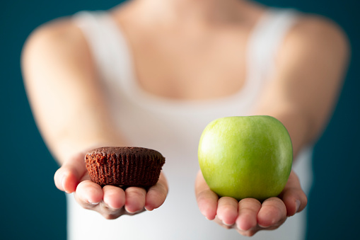 woman holding green apple and chocolate cake in hand, choosing between healthy and junk food,