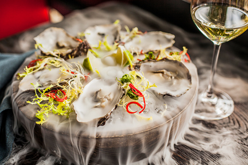 A plate of oysters in smoke and a glass of white wine nearby