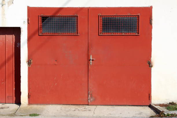 istock Strong old dark red metal garage doors with rusted hinges and windows covered with metal protection net 1304283090