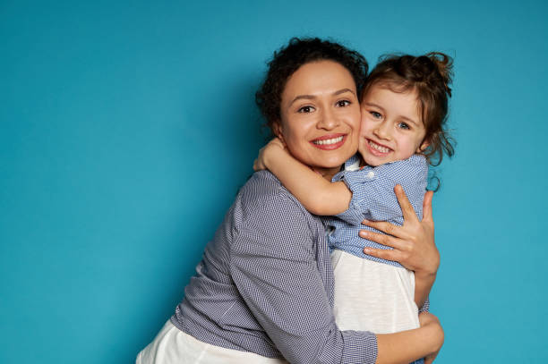 cheerful mother hugging her daughter. blue background, happy mother's day concept, children protection day - family portrait imagens e fotografias de stock