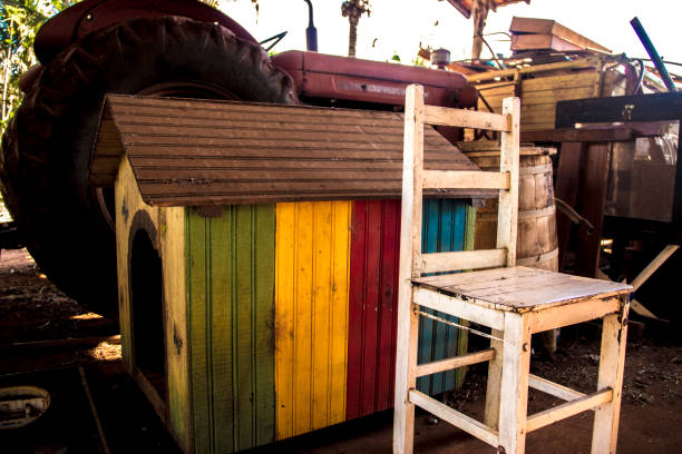Abandoned pile of paraphernalia (chairs, tractor, vibrant colored dog house and more) at a shed