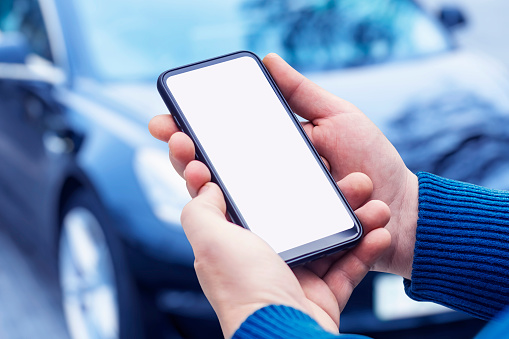 Man holds a smartphone in his hands. Mock up phone with white screen on the background of the car