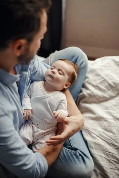 Photo of Middle age Caucasian father with sleeping newborn baby girl. Parent holding rocking a child daughter son in hands. Authentic lifestyle parenting fatherhood moment. Single dad family home life.