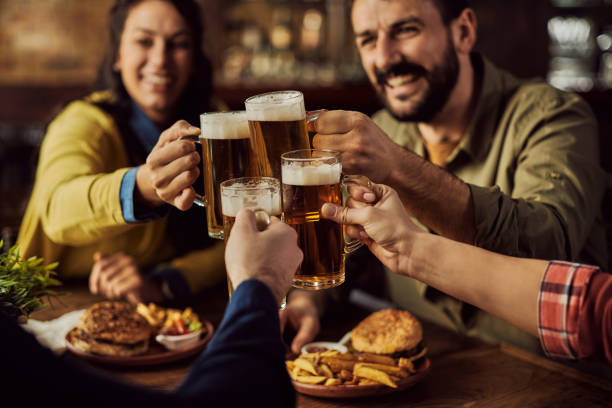 Close-up of friends toasting with beer in a pub. Close-up of group of friends toasting with beer while eating in a pub. pub stock pictures, royalty-free photos & images