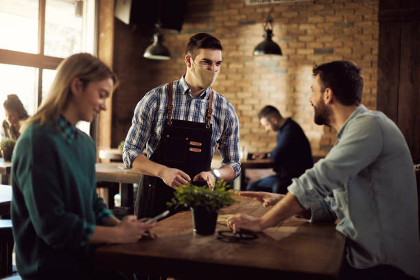 istock Happy waiter wearing face mask while talking to customers n a pub. 1304304550