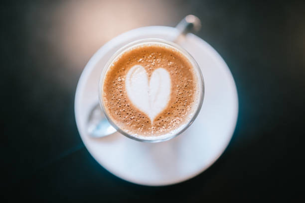 An overhead shot of a mug of espresso and steamed milk on a table, the milk poured into the shape of a heart.